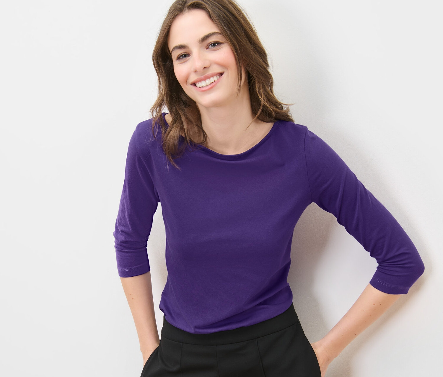 Žena pózuje v fialovom tričku s trojštvrťovým rukávom.