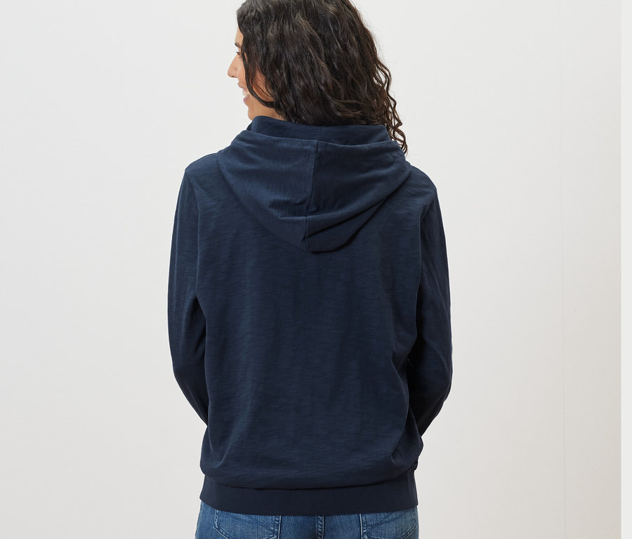 Pohľad zozadu na ženu s tmavými vlasmi v námorníckej modrej džersejovej mikine s kapucňou.