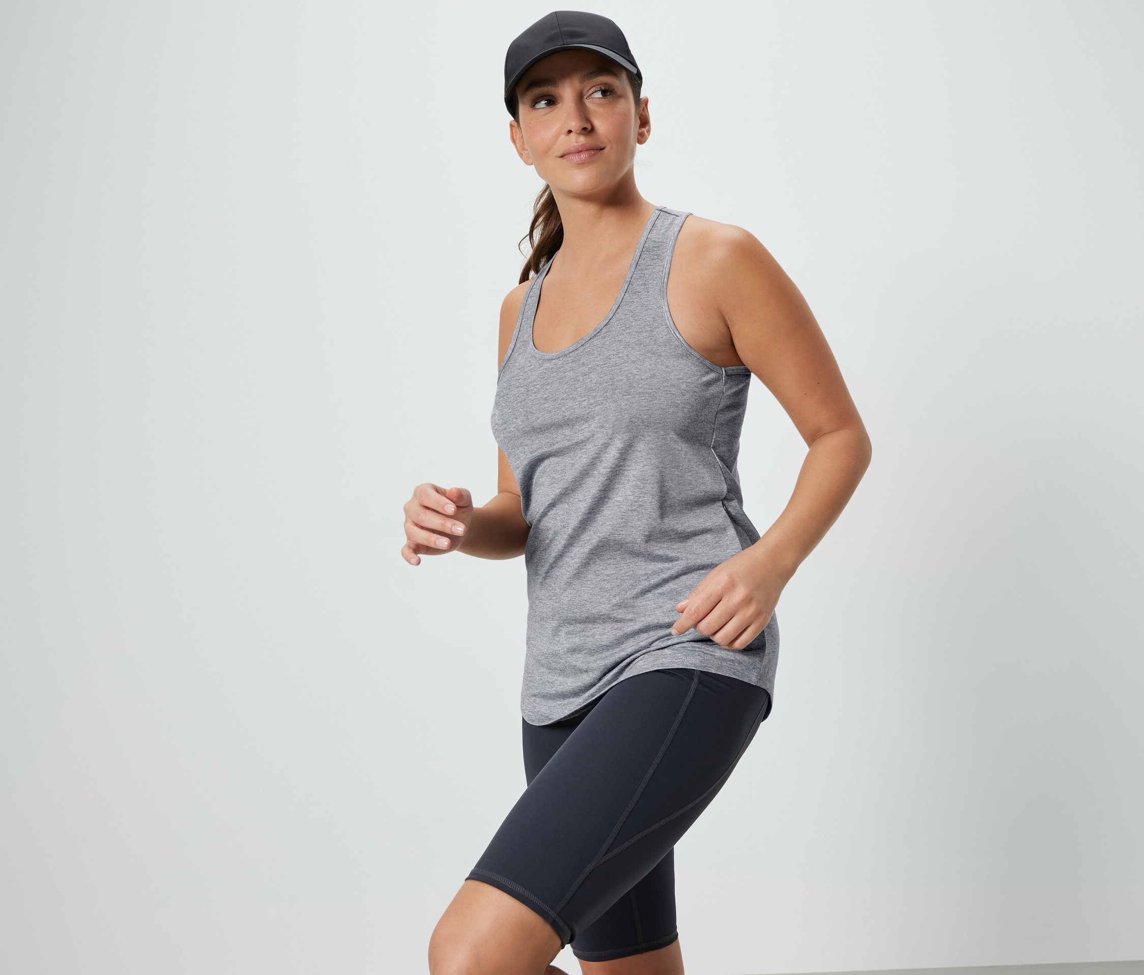 Žena v šedom tope a čiernych športových šortkách s šiltovkou. Funkčné topy, 2 ks, čierny a sivý.