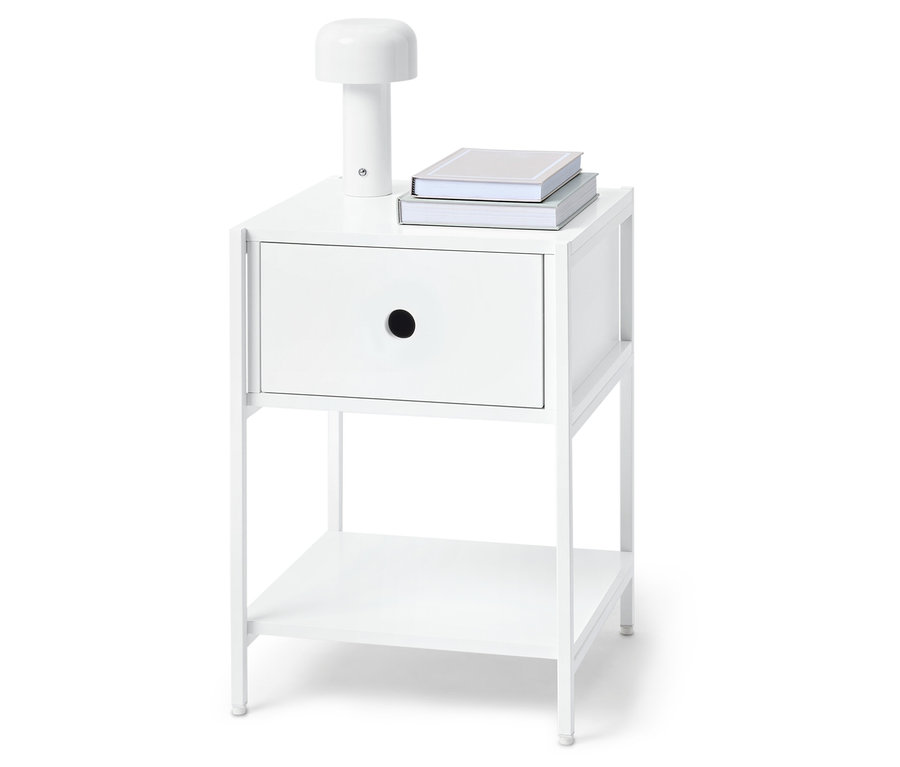 Biely nočný stolík s jednou zásuvkou, lampou a dvoma knihami navrchu.
