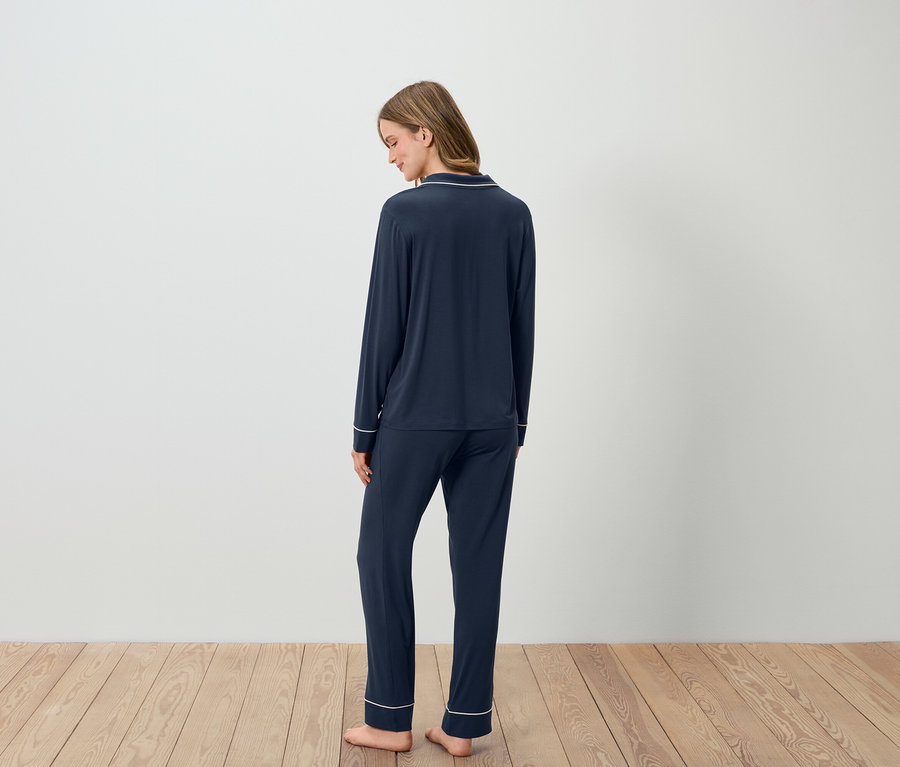 Žena stojí chrbtom, oblečená v tmavomodrom pyžame s bielym lemovaním.