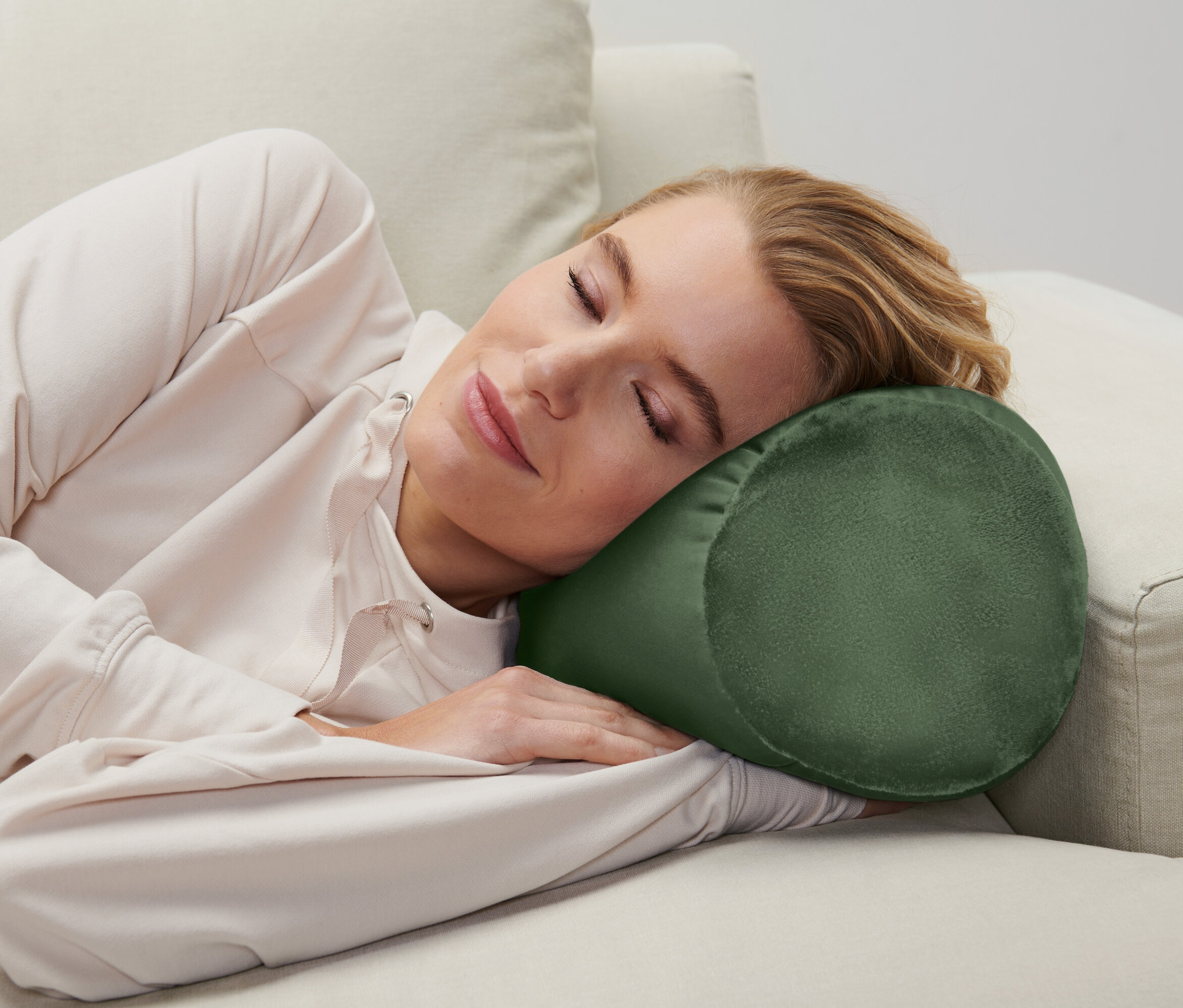 Žena spí na gauči s valcovým vankúšom pod hlavou.