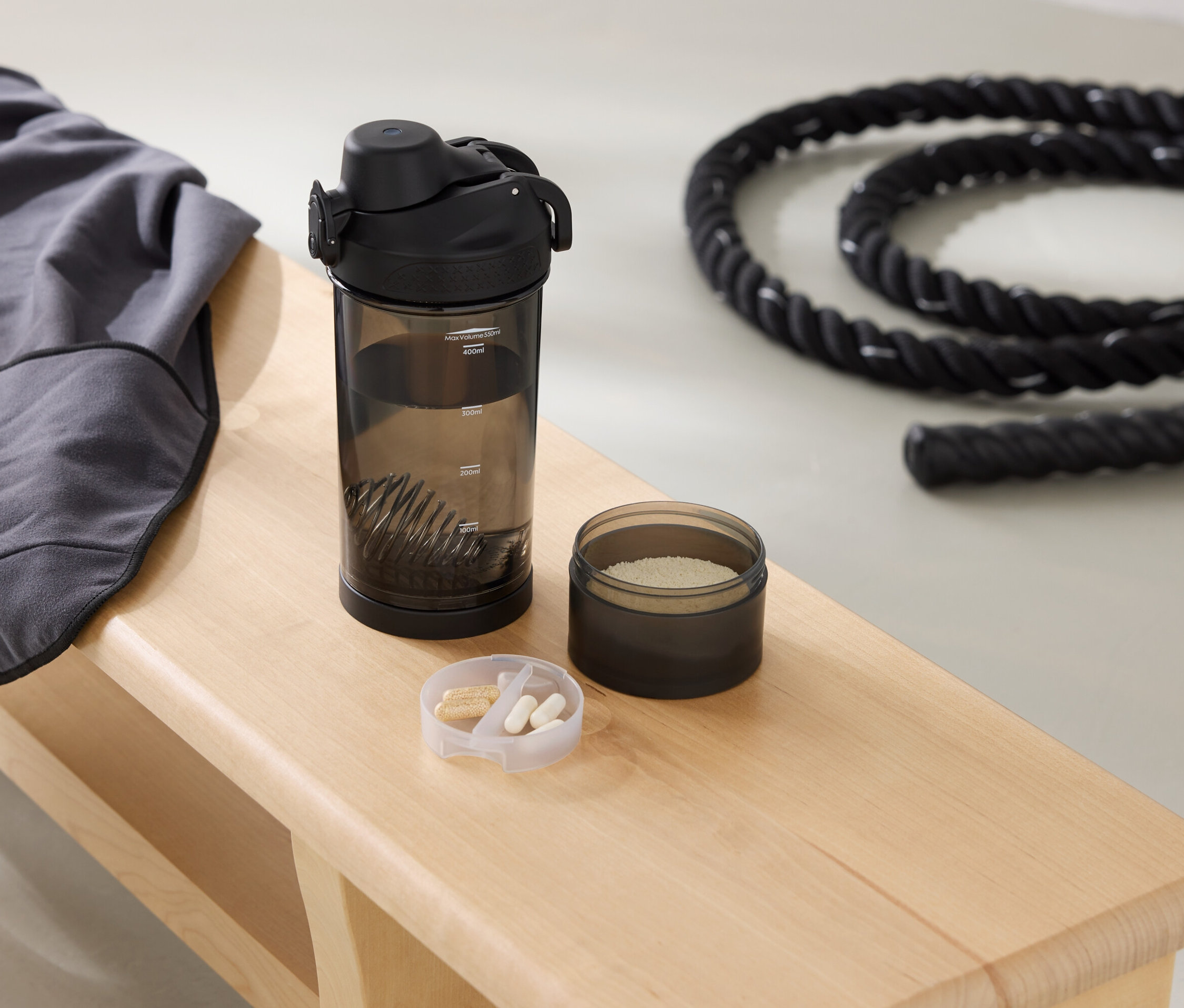 Na lavici leží sivá mikina, fľaša na pitie, dóza s práškom a lano.