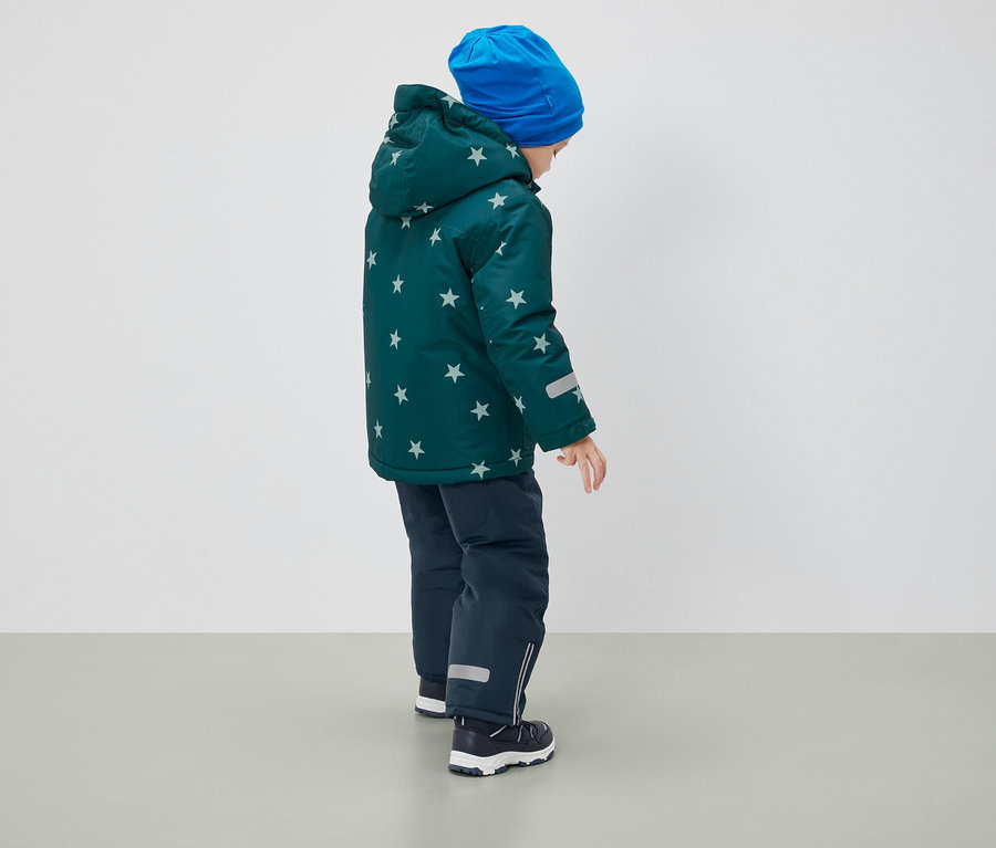 Chlapec chrbtom k fotoaparátu má na sebe zimnú bundu so vzorom hviezd, modrú čiapku a tmavomodré nohavice.