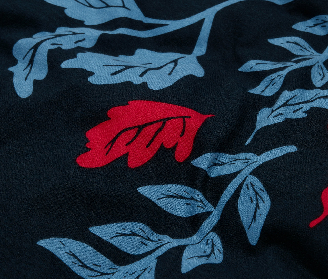 Detailný záber na tmavomodrú látku s celoplošnou potlačou modrých listov a červenými akcentmi.