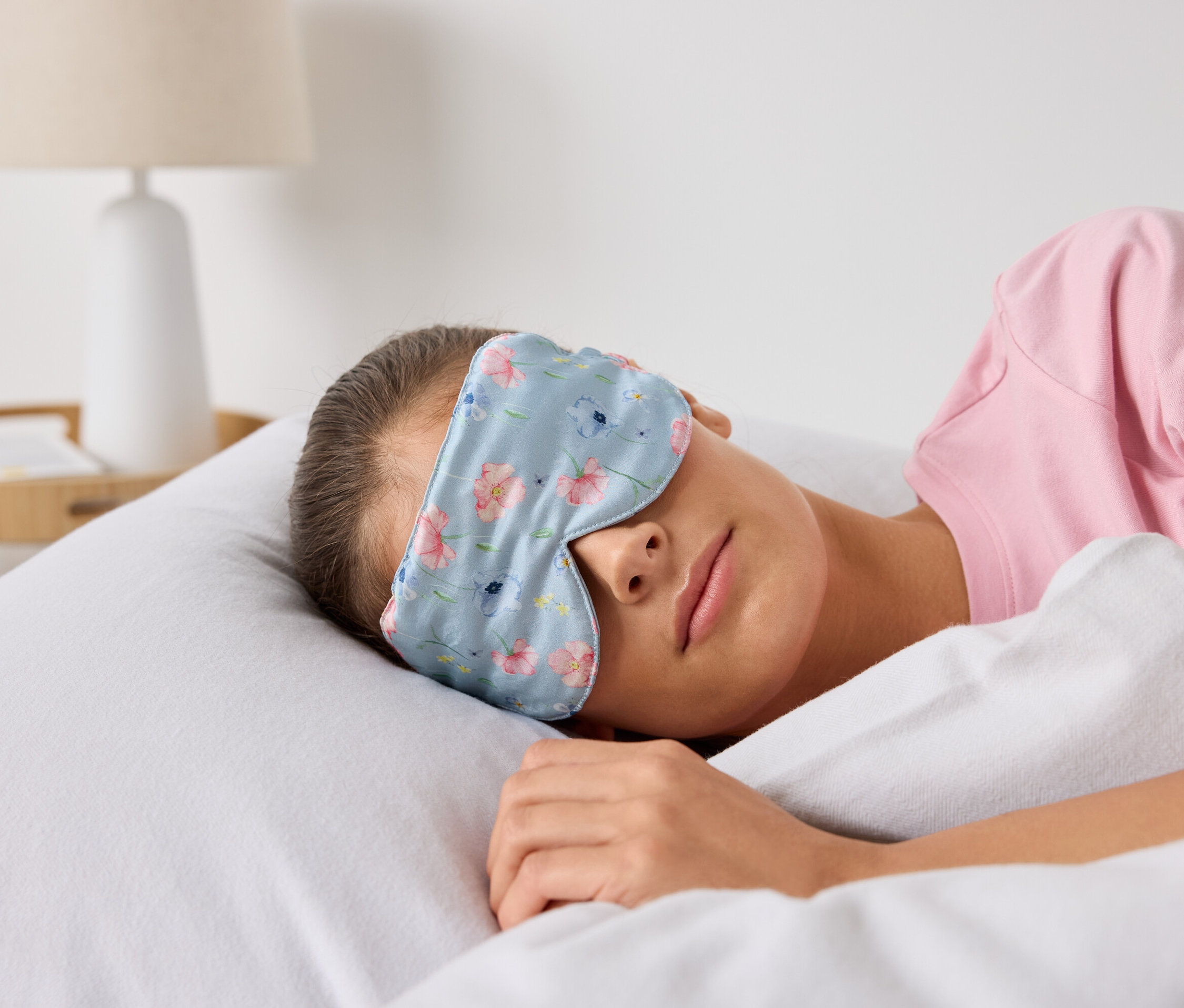 Žena spí v posteli s maskou na spanie s kvetinovým vzorom.