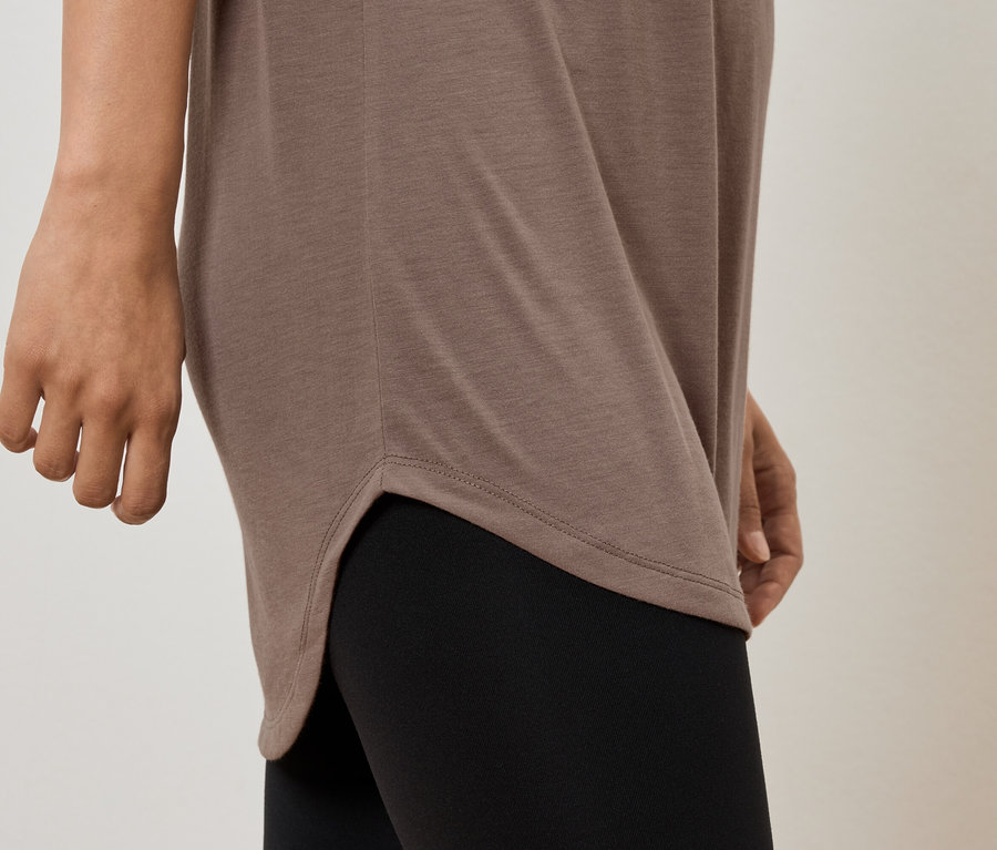 Čiastočný pohľad na ženu v hnedej tunike a čiernych legínach.