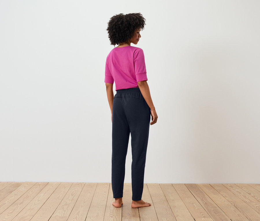 Pohľad zozadu na ženu s afro účesom, ktorá má na sebe ružové tričko a tmavomodré nohavice.