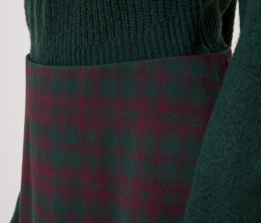 Detail dámskeho outfitu so zeleným svetrom a kockovanou sukňou.