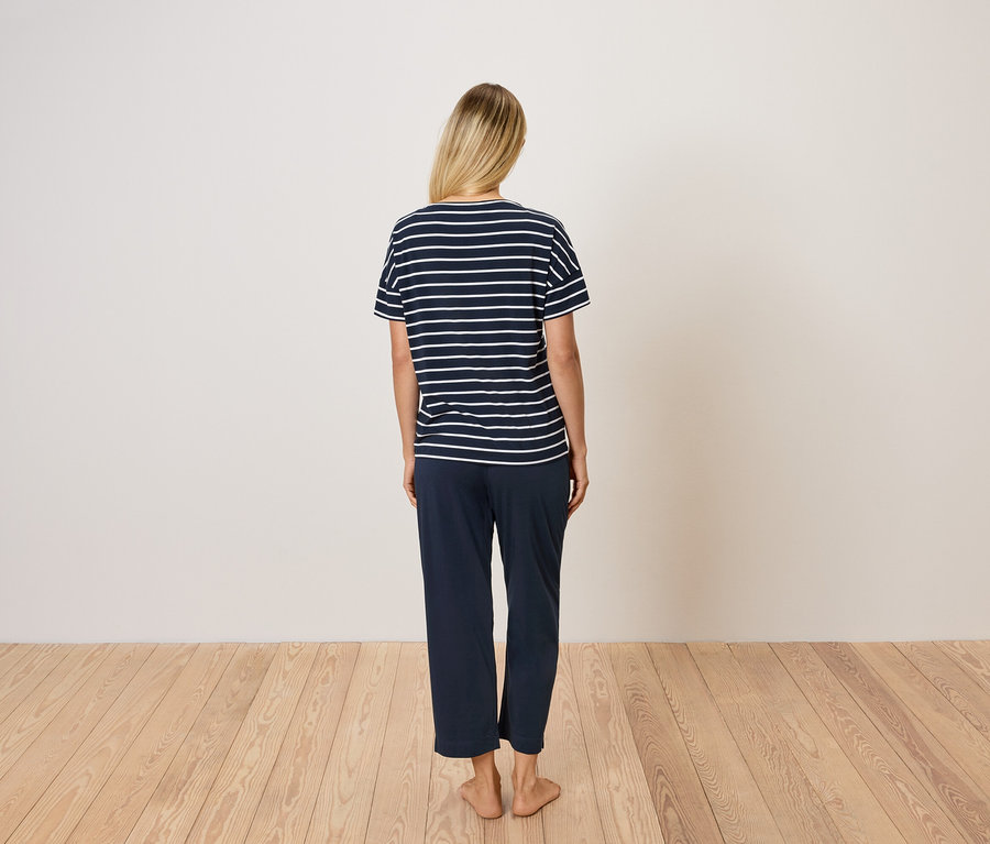 Pohľad zozadu na ženu s blond vlasmi v modrom pruhovanom tričku a modrých nohaviciach.