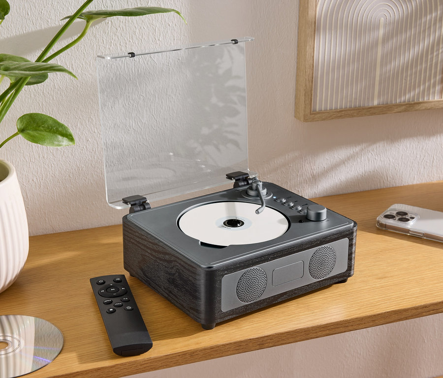 Na stole stojí reproduktor CD/Bluetooth® s CD, diaľkovým ovládačom a mobilným telefónom.