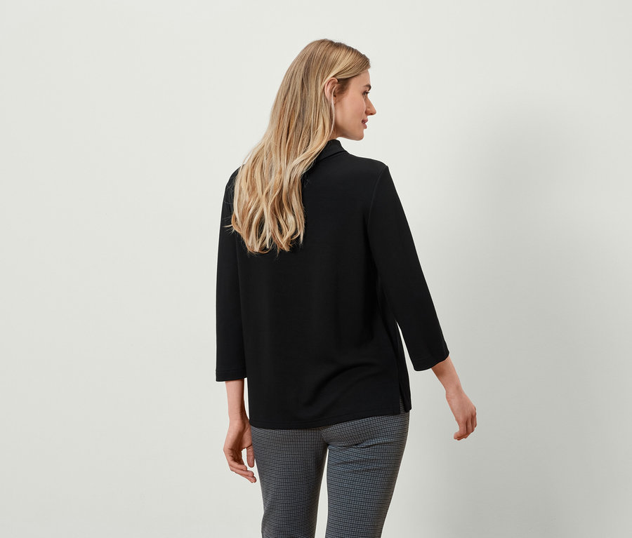 Zozadu blondína v čiernom tope s trojštvrťovými rukávmi a sivých kockovaných nohaviciach.