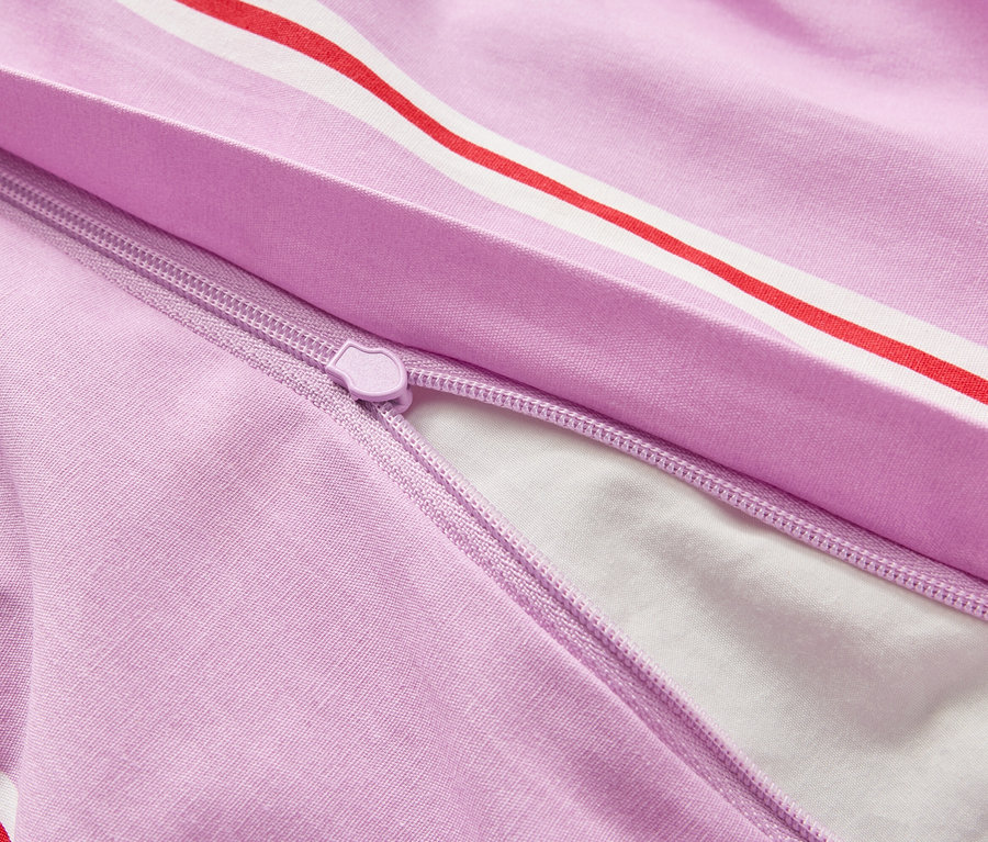 Detailný záber na čiastočne otvorenú, fialovú obliečku na prikrývku s červeno-bielymi pruhmi a zipsom, ktorý odhaľuje biely vnútrajšok.