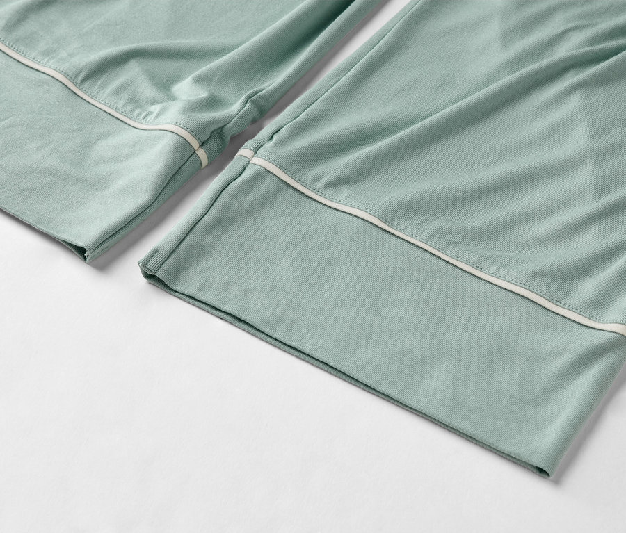 Detailný záber svetlozelených pyžamových nohavíc s bielym lemovaním na leme.
