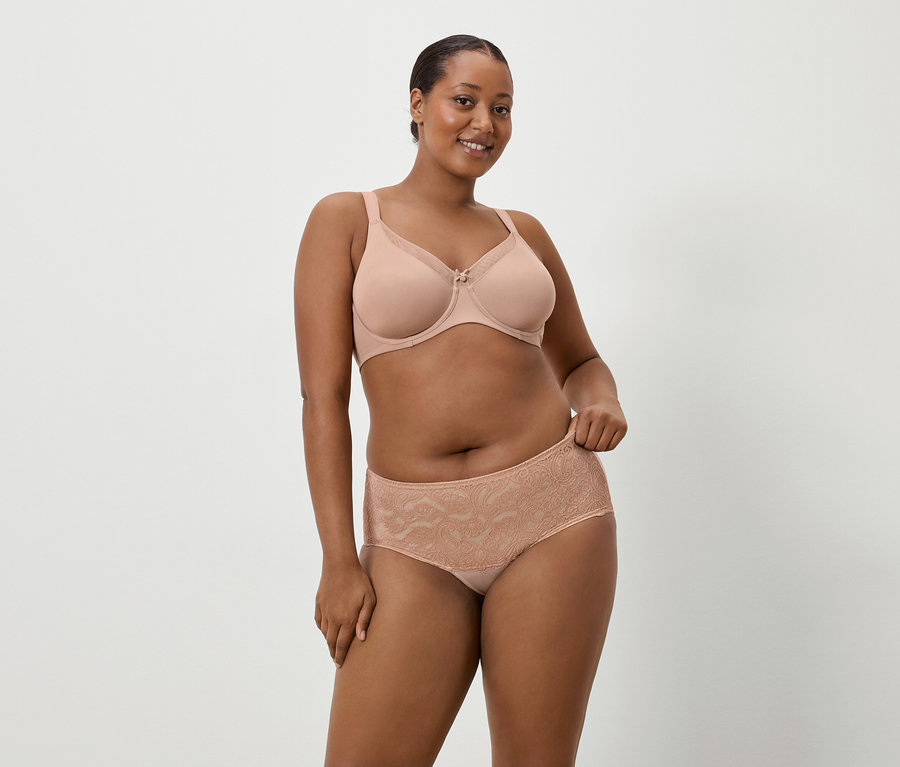 Žena tmavej pleti má na sebe telovú podprsenku a zodpovedajúce čipkované nohavičky na jednoduchom pozadí.