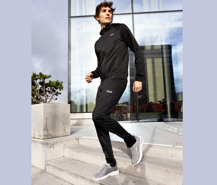 Muž v čiernej teplákovej súprave Fila a sivých teniskách schádza po betónových schodoch.