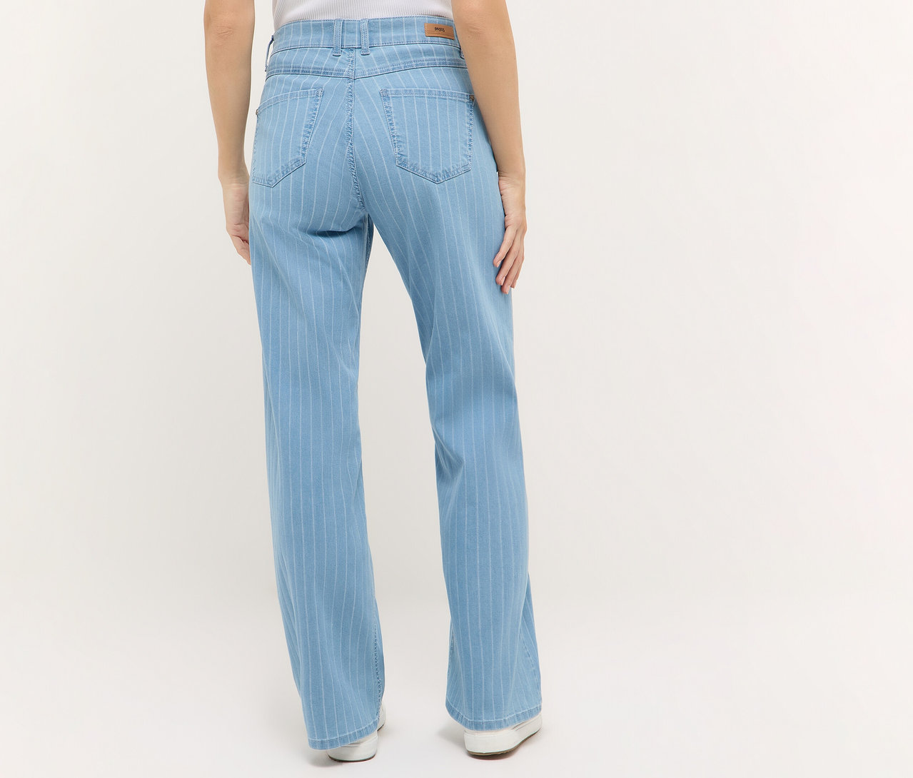 Pohľad zozadu na ženu v džínsoch Angels Denim »Liz«, Wide Leg so svetlými pruhmi a bielych topánkach na svetlom pozadí.