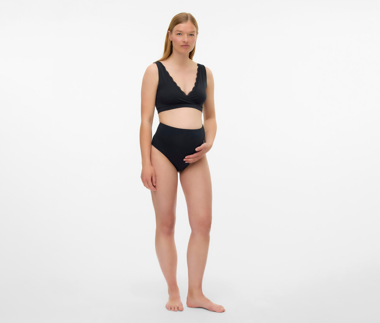 Tehotná žena má na sebe čiernu tehotenskú podprsenku MAMALICIOUS »MLHELENA«, 2 ks a nohavičky s vysokým pásom na bielom pozadí.