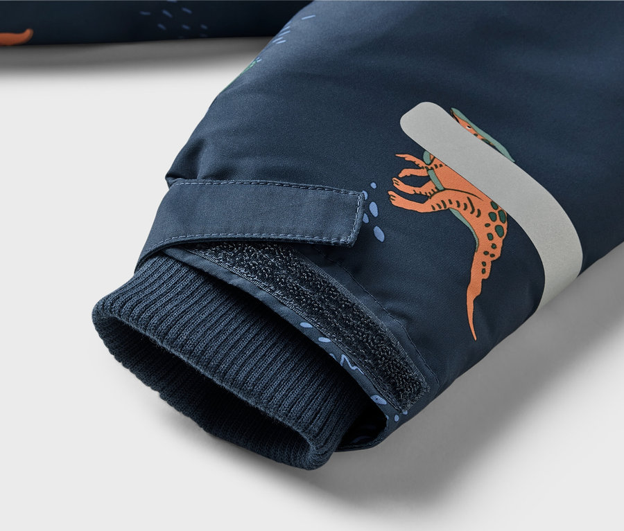 Detail rukáva tmavomodrej bundy s dinosím vzorom, rebrovaným lemom a zapínaním na suchý zips.