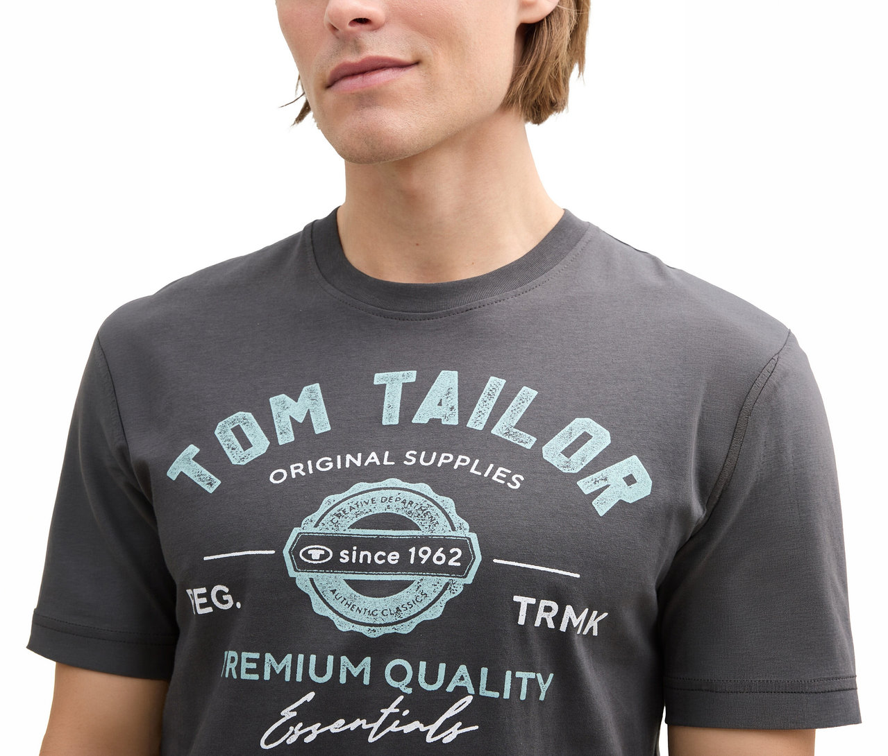 Muž má na sebe sivé tričko Tom Tailor s logom, tmavosivá.