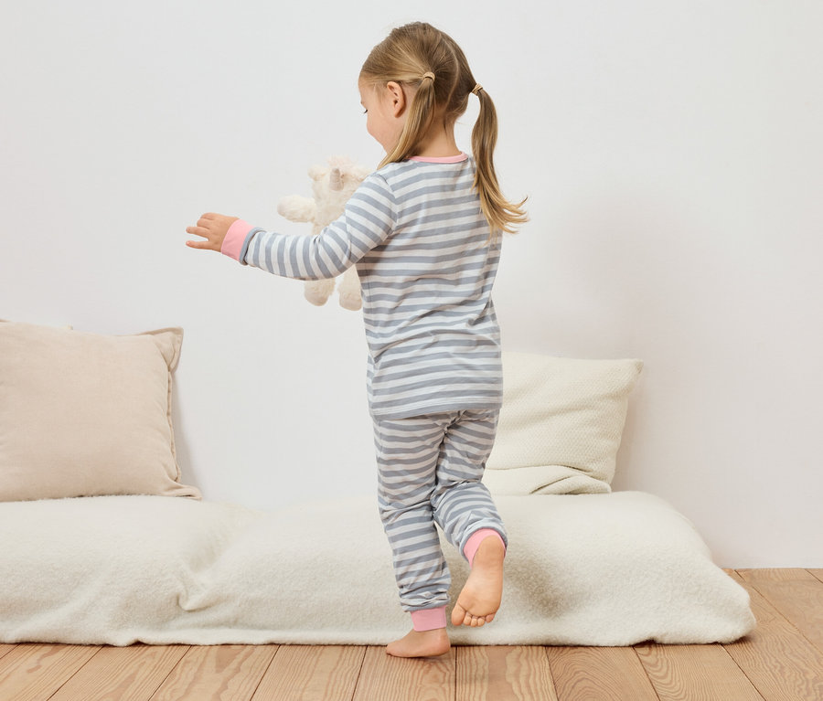 Dievča v sivo-bielom pásikavom pyžame drží plyšového medveďa na gauči.