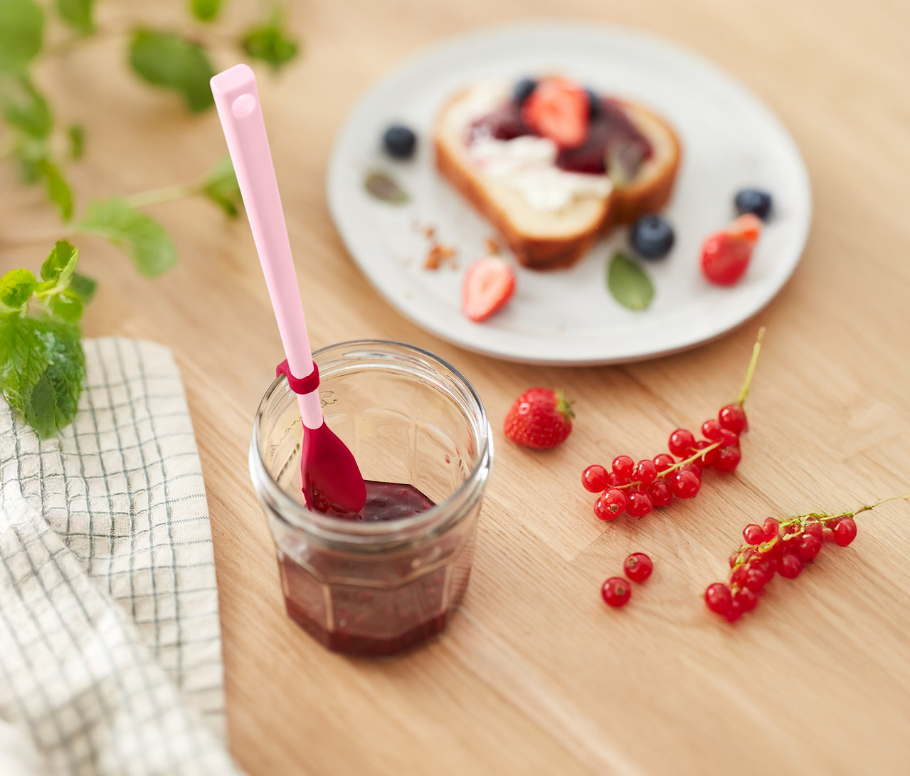 Pohár džemu s ružovou lyžičkou, toast s jahodami a čučoriedkami a ríbezle na drevenom stole.