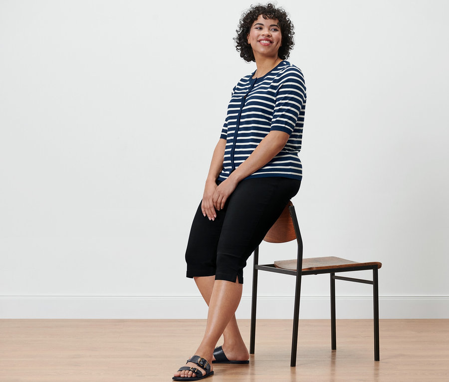 Žena sedí na stoličke a má na sebe 3/4 bengalínové nohavice, čierne.