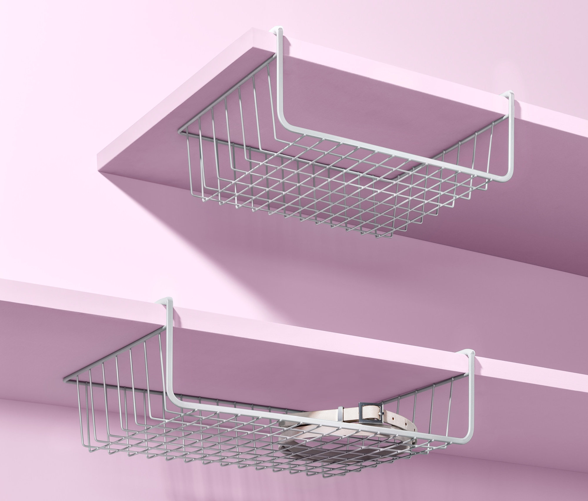 Dva kovové košíky do skrine sú zavesené pod policami na ružovom pozadí.