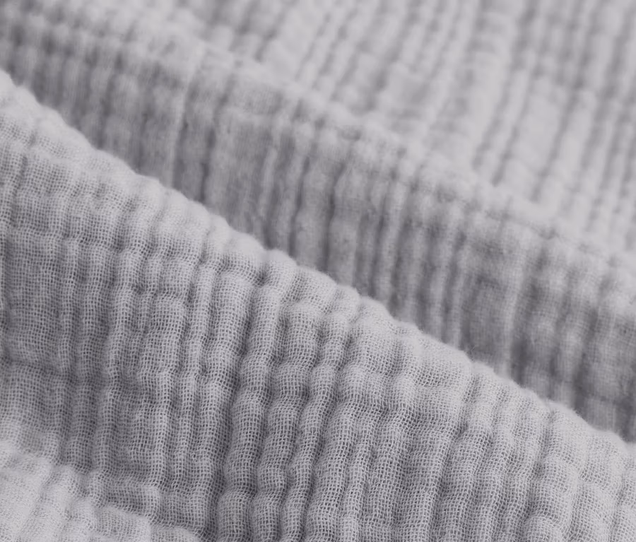 Detailný záber na sivú mušelínovú posteľnú bielizeň štandardnej a nadmernej veľkosti.