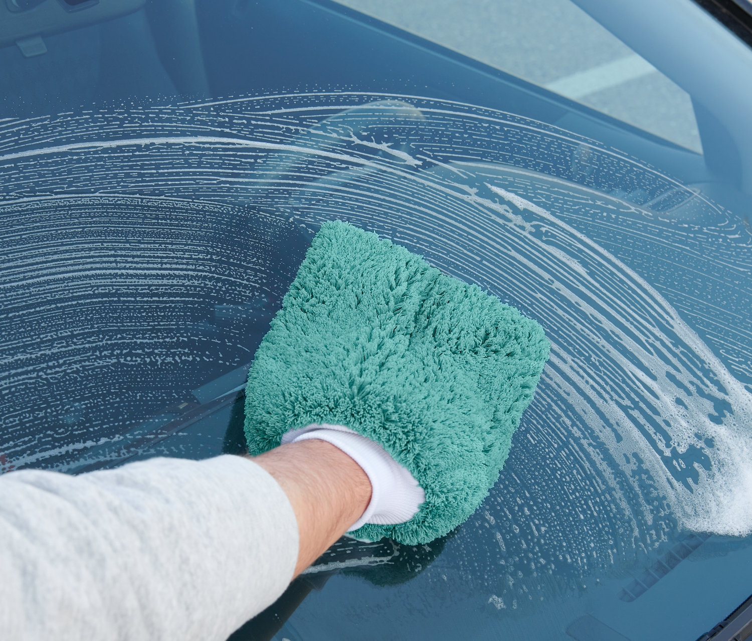 Muž umýva čelné sklo auta pomocou rukavice na umývanie auta.