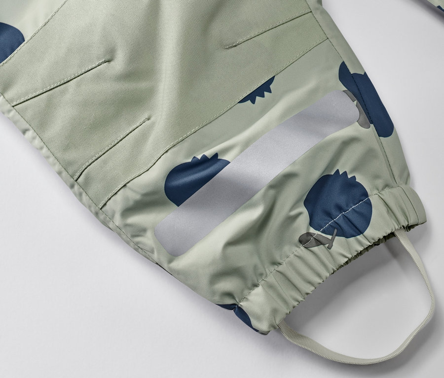 Detail detského overalu do dažďa so vzorom čučoriedok, reflexným pruhom a elastickým lemom.