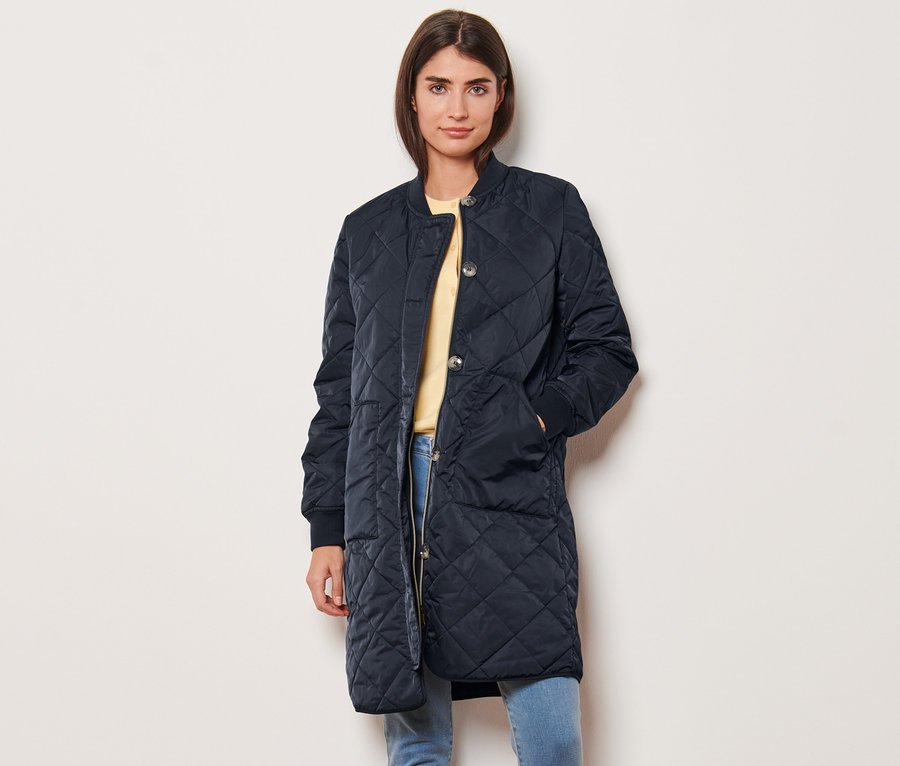 Žena pózuje v prešívanom kabáte.