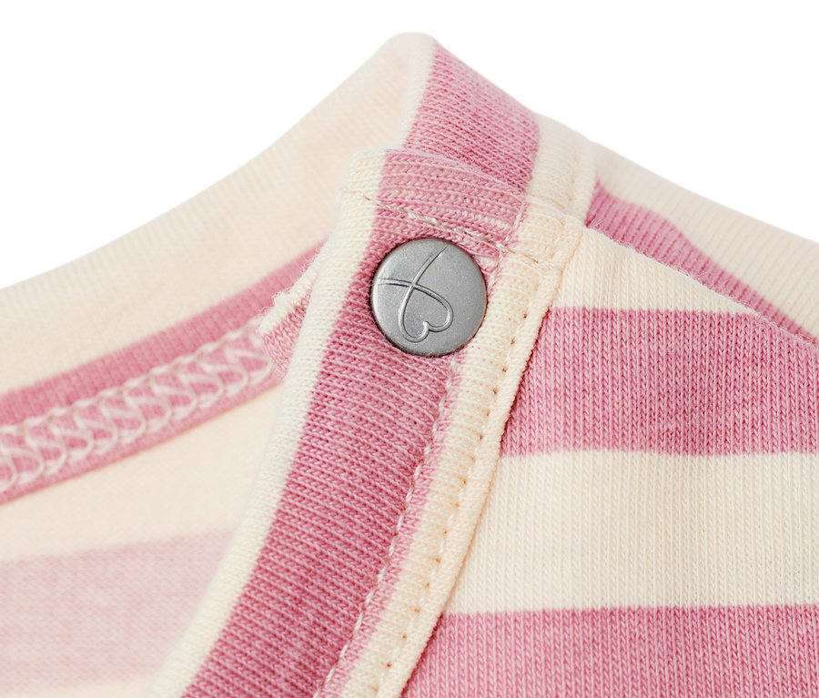 Detail detských džersejových šiat s ružovými a krémovými pruhmi a strieborným gombíkom v tvare srdca.