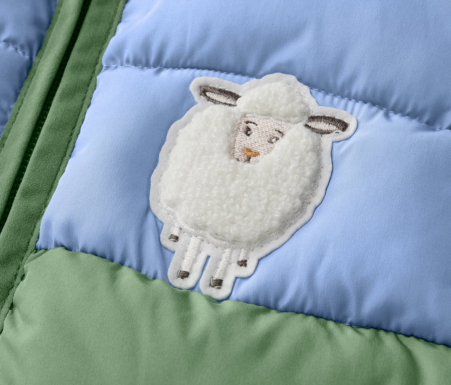 Detail detskej prešívanej vesty s color blockingom a nášivkou ovečky.