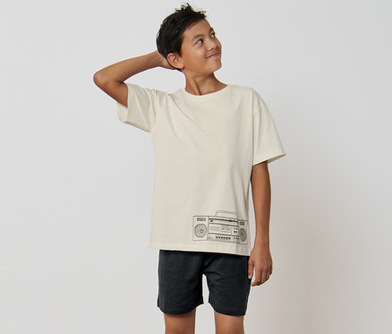 Chlapec v detskom pyžame so vzorom rádia stojí bosý v miestnosti.