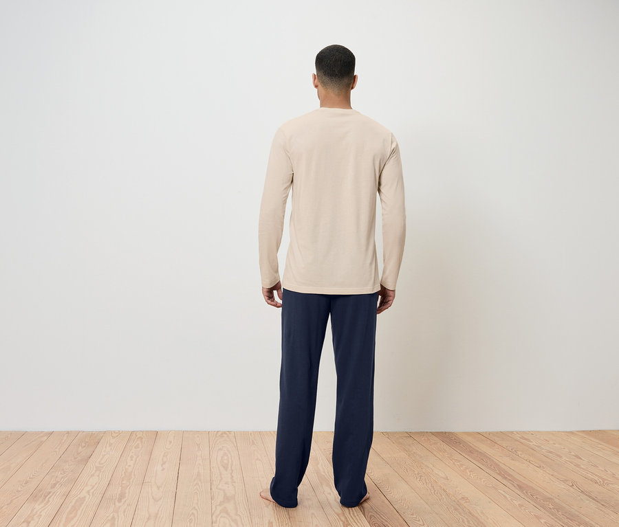 Muž chrbtom k fotoaparátu má na sebe béžové tričko s dlhým rukávom a tmavomodré nohavice.