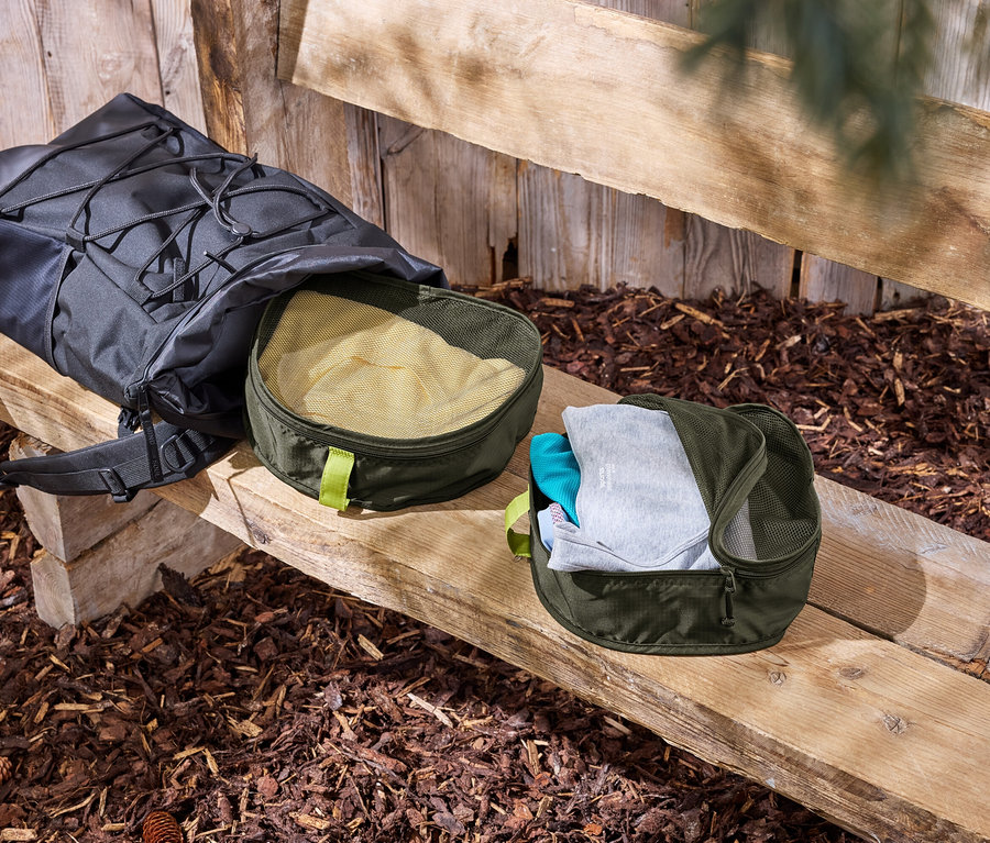 Čierny batoh leží na drevenej lavici vedľa dvoch zelených organizérov na oblečenie.