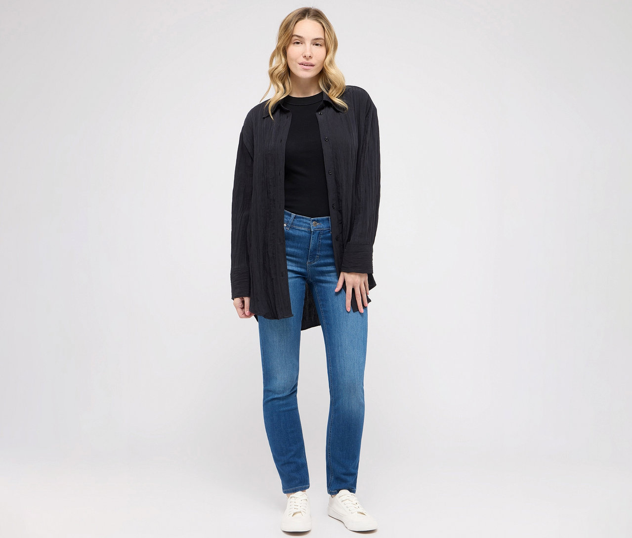 Žena pózuje v slim fit džínsoch Angels »Cici« modrej farby, čiernom tričku a blúzke.