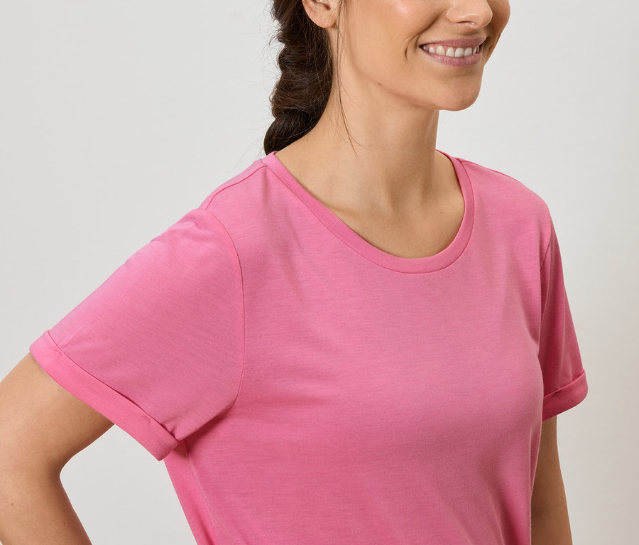 Žena s hnedými vlasmi a úsmevom má na sebe ružové tričko.