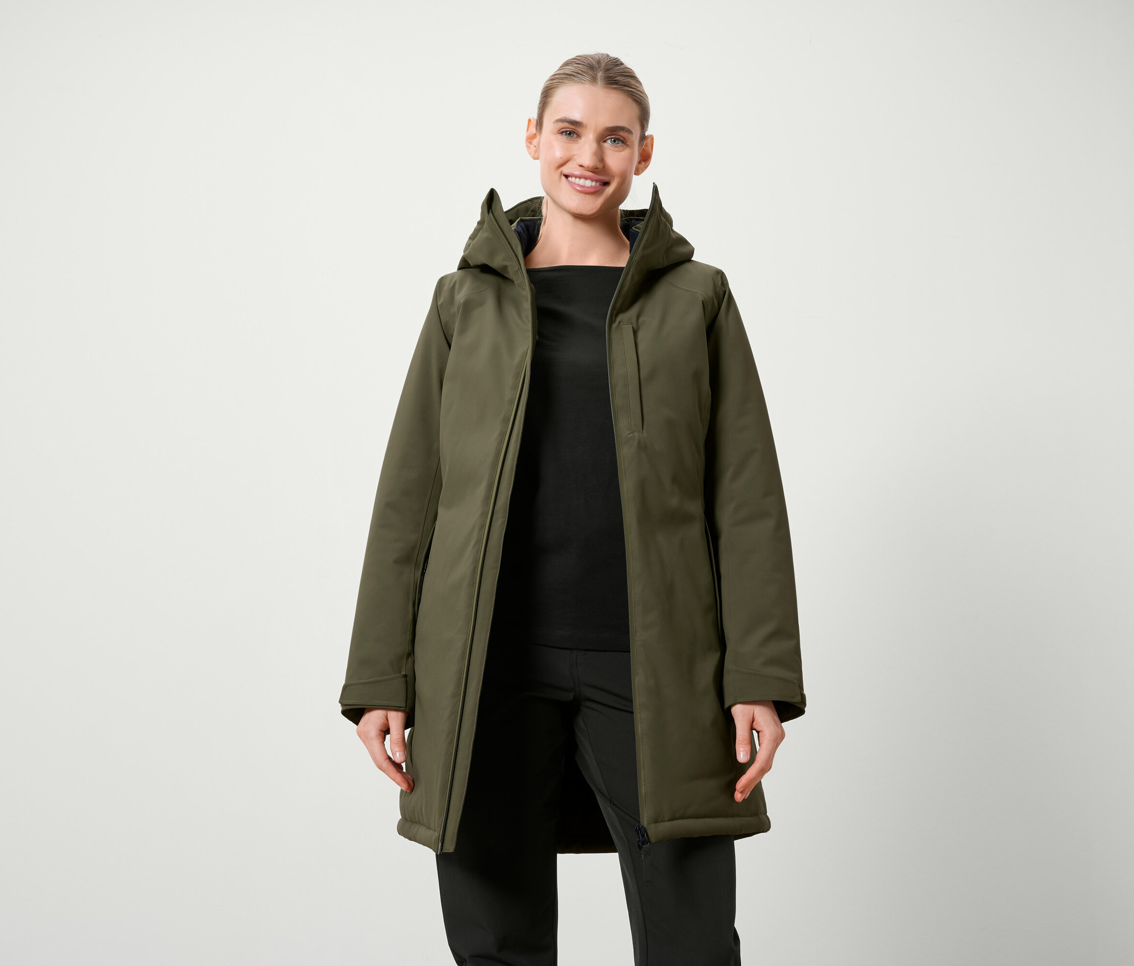 Žena pózuje v olivovo zelenej bunde s kapucňou a čiernom oblečení.