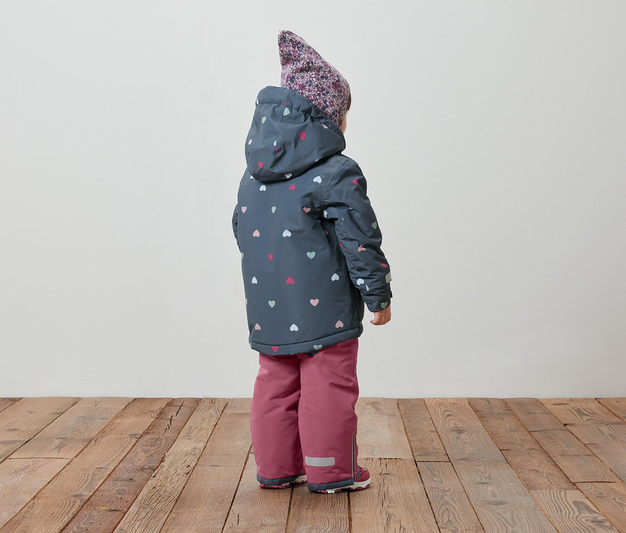 Pohľad zozadu na dieťa v zimnej bunde s kapucňou so vzorom srdiečok a v ružových otepľovačkách.