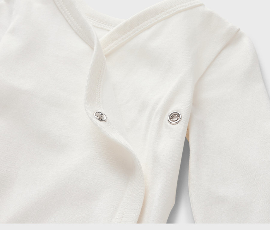 Detail bieleho body pre bábätká s dlhým rukávom a zapínaním na patentky.