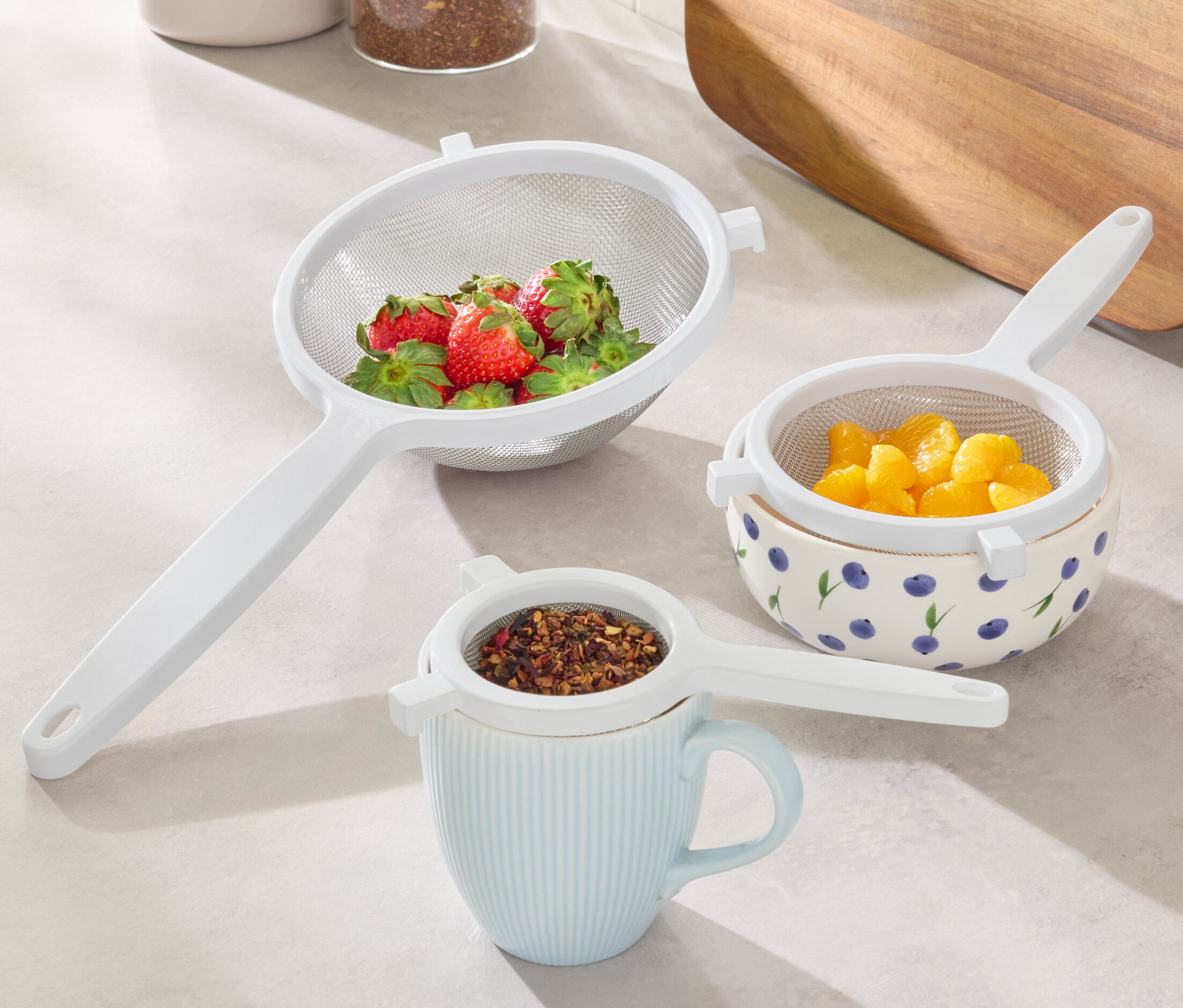 Sada cedidiel: Cedidlo s jahodami, cedidlo s pomarančmi v miske s čučoriedkami, cedidlo s čajom na hrnčeku.