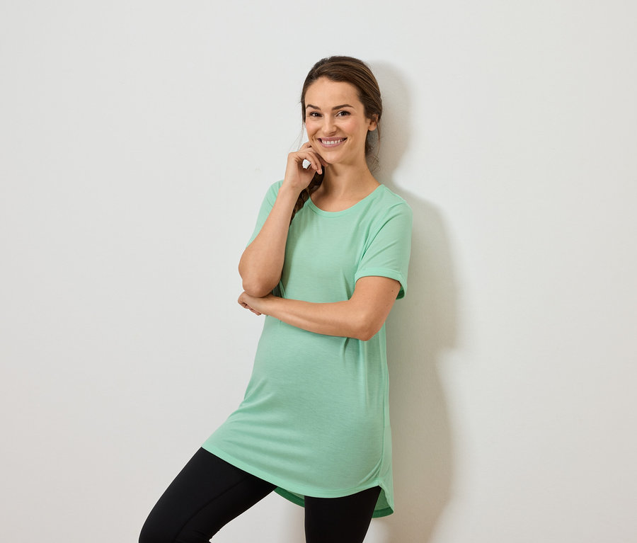 Žena v mätovo zelenom tope a čiernych legínach pózuje s rukou na brade.