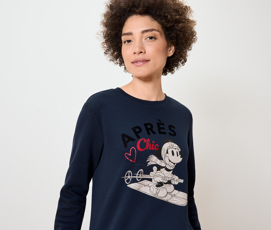 Žena má na sebe tmavomodrý sveter s potlačou Mickey Mousa na snowboarde.