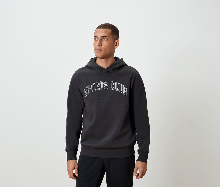 Muž má na sebe tmavosivú mikinu s kapucňou a nápisom SPORTS CLUB.