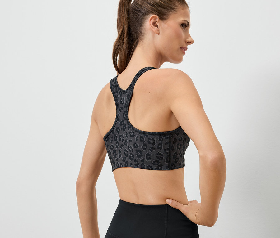 Žena chrbtom k fotoaparátu má na sebe športovú podprsenku so zvieracím vzorom a čierne legíny.