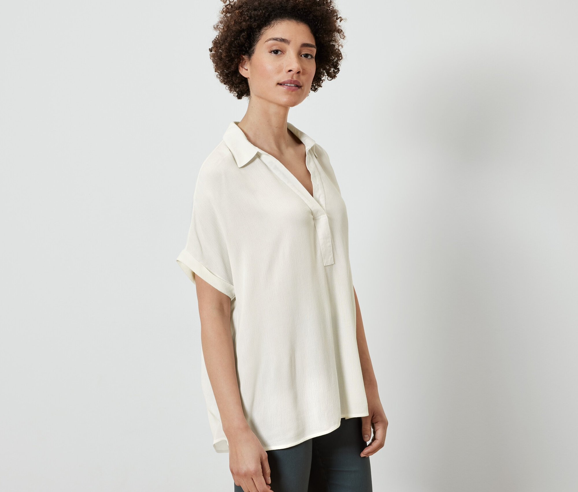 Žena pózuje v krémovobielej blúzke.
