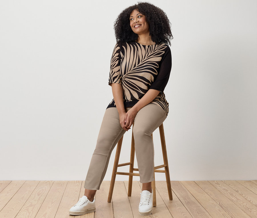 Žena sedí na stoličke a má na sebe 7/8 tregínsy, top s potlačou a tenisky.