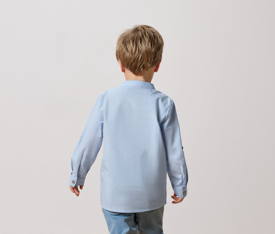 Pohľad zozadu na dieťa s blond vlasmi v svetlomodrej košeli a džínsoch.
